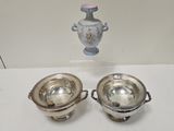 two silver dishes on a table with a vase in the background