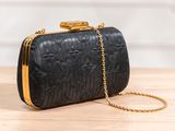 a black clutch bag with gold chain on a wooden table
