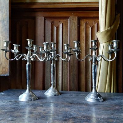 trois chandeliers en argent posés sur une table devant une fenêtre