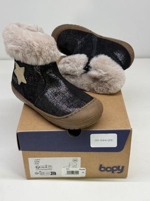 des bottines noires et blanches pour bébé, doublées de fourrure, posées sur une boîte en carton