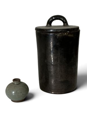 un récipient noir et un vase vert posés sur une surface blanche