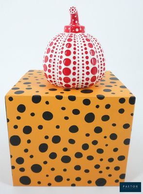 a red and black polka dot vase sitting on top of a yellow box