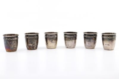 six verres à shot en argent alignés sur une surface blanche