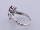 a close up of a diamond and ruby ring on a white surface
