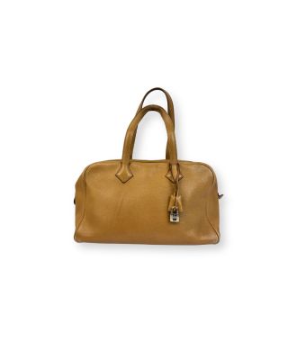 Le sac à main en cuir beige est posé sur une surface blanche.