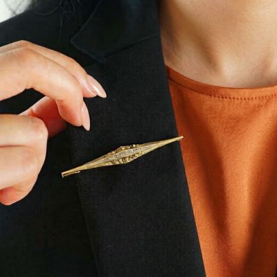 une femme vêtue d'un blazer noir et d'une chemise orange, tenant une broche dorée