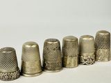 six antique thimbles lined up in a row on a white surface