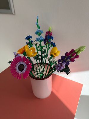 des fleurs aux couleurs vives dans un vase blanc posé sur une table rouge