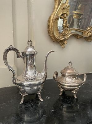 deux théières en argent posées sur une table à côté d'un miroir