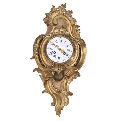 a gold clock hanging on the wall with a white background