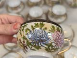 a person holding a tea pot in front of a table full of tea cups and saucers