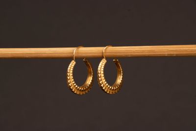 une paire de boucles d'oreilles créoles en or suspendues à un bâton en bois