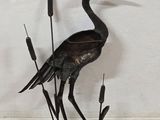 a metal sculpture of a crane standing on top of a pond