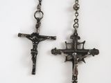 two silver crosses hanging from a chain on a white surface