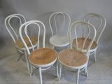 quatre chaises blanches avec une assise en osier, alignées contre un mur blanc