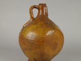 un vieux vase marron muni d'une anse, posé sur une surface blanche