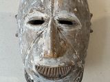 un masque en bois accroché à un mur sur fond blanc