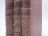 trois vieux livres sont empilés sur une surface blanche