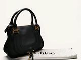 the small black purse is next to a white bag on a white surface
