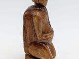 an old wooden figurine of a man sitting on a stool