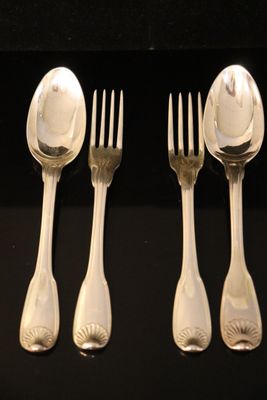 quatre cuillères en argent et une fourchette sont alignées sur une surface noire