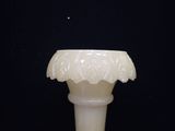a white vase with a flower on it on a black surface