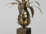 une image représentant un vase en laiton orné d'un ananas, posé sur un socle en bois