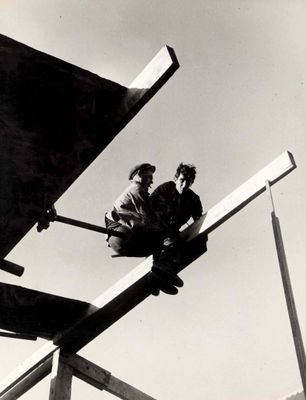 two men sitting on top of a building under construction
