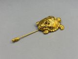 un gros plan d'une broche en forme de tortue dorée posée sur une surface grise