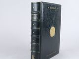 un vieux livre noir aux tranches dorées posé sur une surface blanche