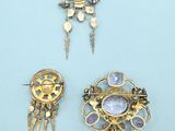three gold and silver brooches and earrings on a blue surface
