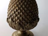 une petite pomme de pin posée sur un socle, sur une surface blanche