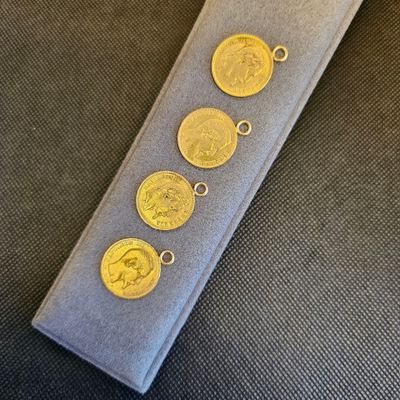 trois breloques en forme de pièces d'or sur une cravate grise sur fond noir