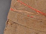 a piece of brown paper with red thread on top of it