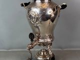 une urne ancienne en métal argenté, posée sur un socle, sur une table