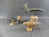 three carved birds are sitting on a wooden stand on a gray background