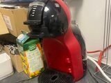 une cafetière rouge posée sur un plan de travail, à côté d'une grille métallique
