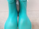 pair of turquoise rain boots with white soles on a beige surface
