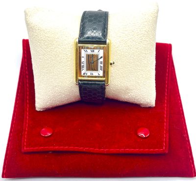 une petite montre carrée posée sur un coussin rouge, à côté d'un oreiller blanc