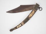 an old knife with gold decoration on it sitting on top of a white surface