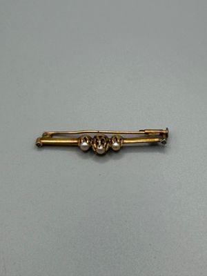 an image of a gold pin with pearls on it on a gray surface