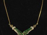 a gold necklace with green and white stones on a black mannequin