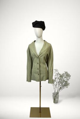 mannequin wearing a green jacket and black hat with a flower in a vase