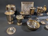 several silver dishes and cups on a table with a black background