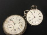 two silver pocket watches sitting on a black surface