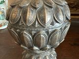 un vase en argent posé sur une table, avec un miroir en arrière-plan