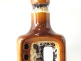 une bouteille marron percée d'un trou, posée sur une surface blanche