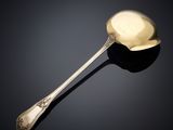 une cuillère ancienne en argent dont le manche repose sur une surface noire