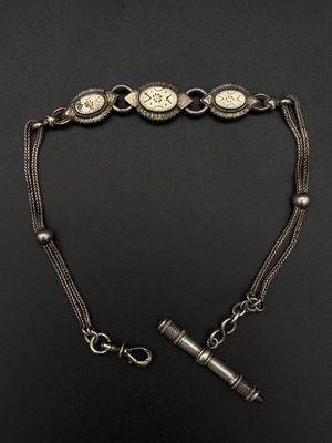 un vieux bracelet en argent avec une montre et un briquet posés sur une surface noire