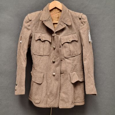Une veste marron est suspendue à un cintre accroché à un mur gris.